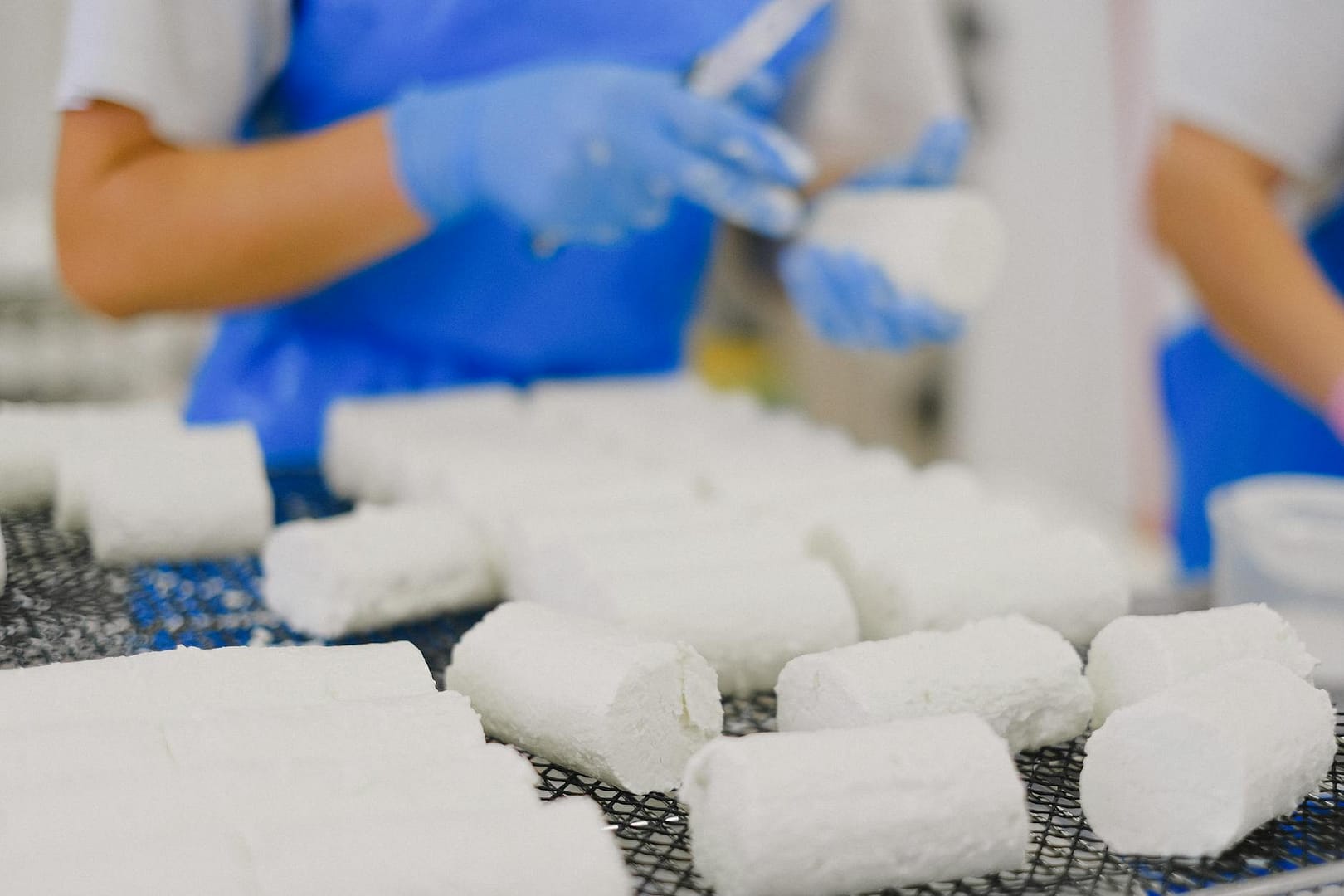close up of white cheese in a factory and workers in blue aprons in background